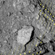 Close-up of Ryugu’s surface with arrows pointing to a rugged, layered boulder.